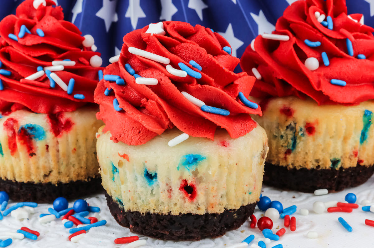 Closeup on three Patriotic Brownie Cupcakes sitting on a white table covered in Red White and Blue sprinkles.