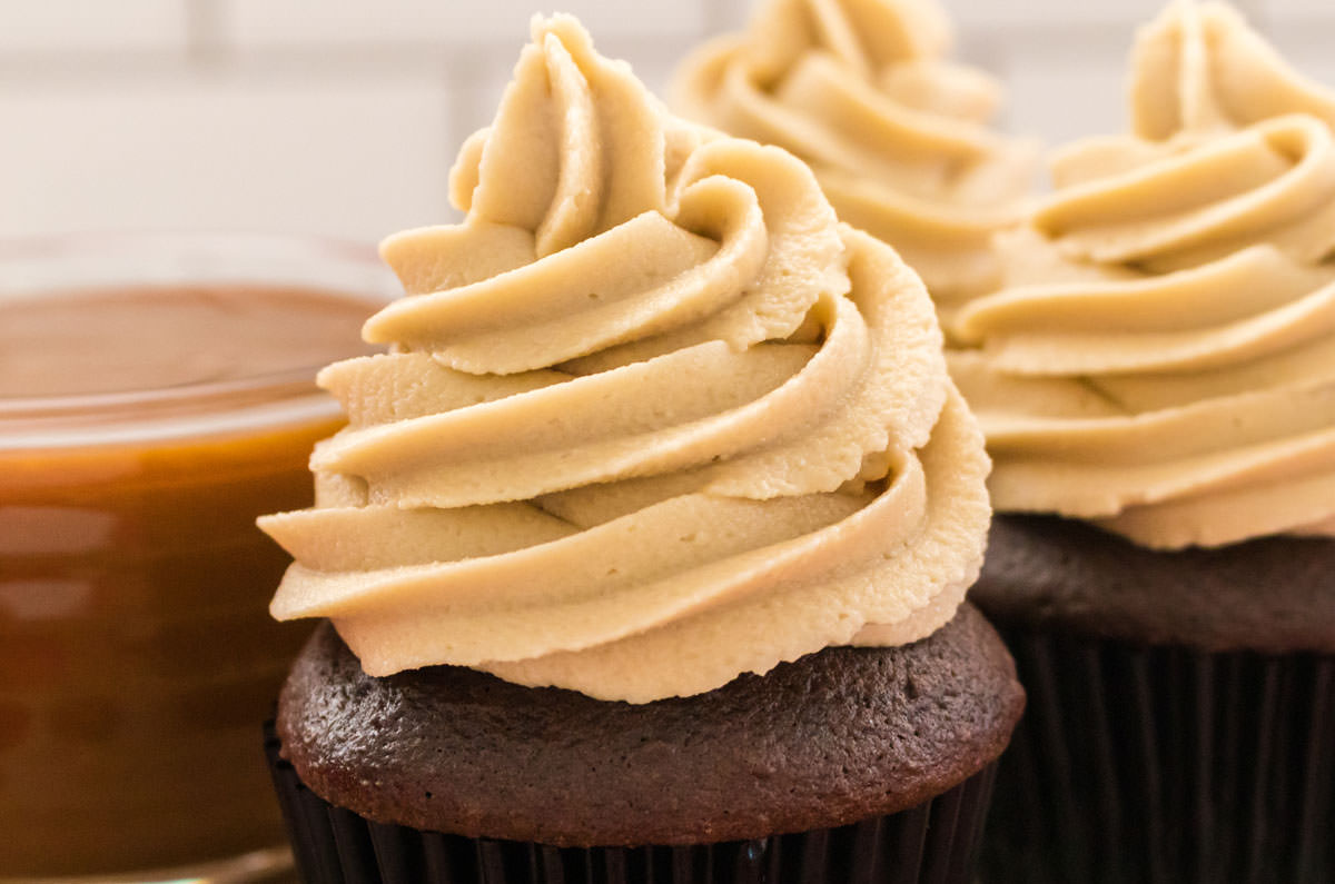 Closeup on three chocolate cupcakes frosted with a swirl of The Best Caramel Buttercream Frosting.