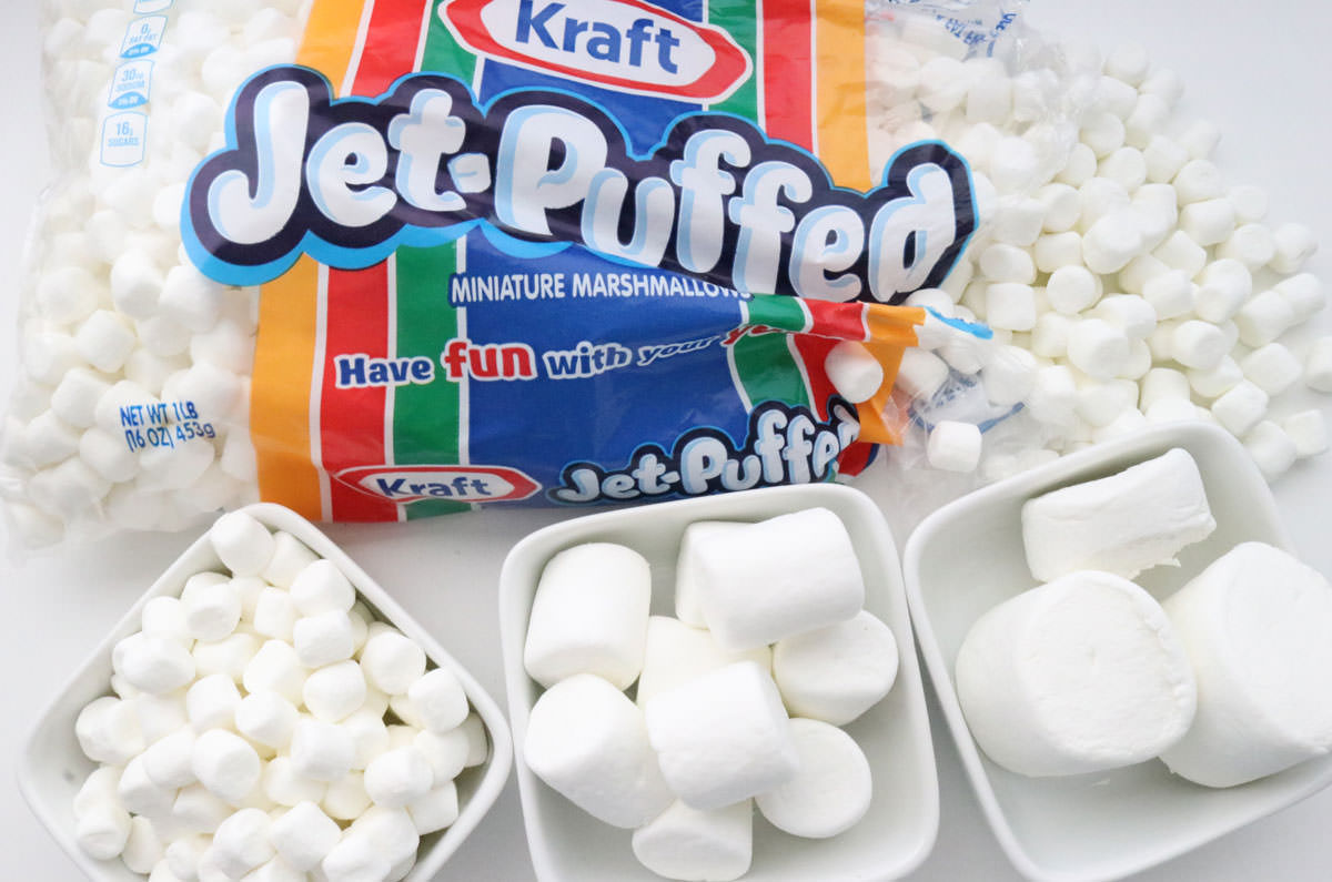 An opened bag of mini marshmallows and three ramekins filled with other sizes of marshmallows to show how many mini marshmallows equal to regular sized marshmallows and jumbo marshmallows.