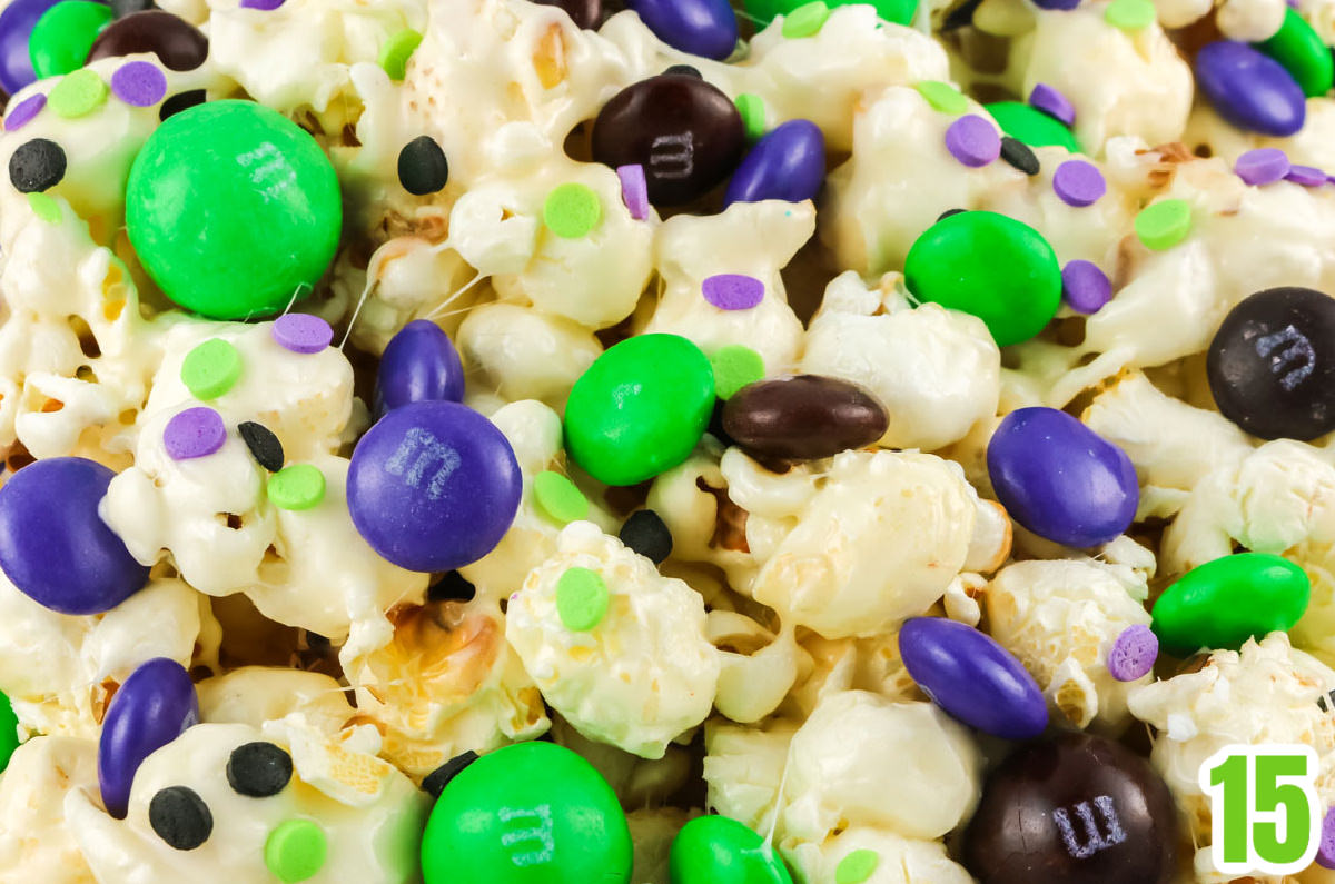 Closeup of a batch of Bewitched Halloween Popcorn showing the marshmallow popcorn sprinkled with Halloween colored M&M's and sprinkles.