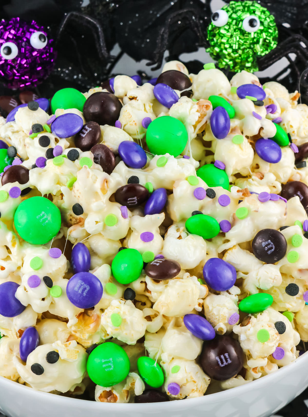 Closeup on Bewitched Halloween Popcorn in a white serving bowl sitting in front of Halloween Decorations.
