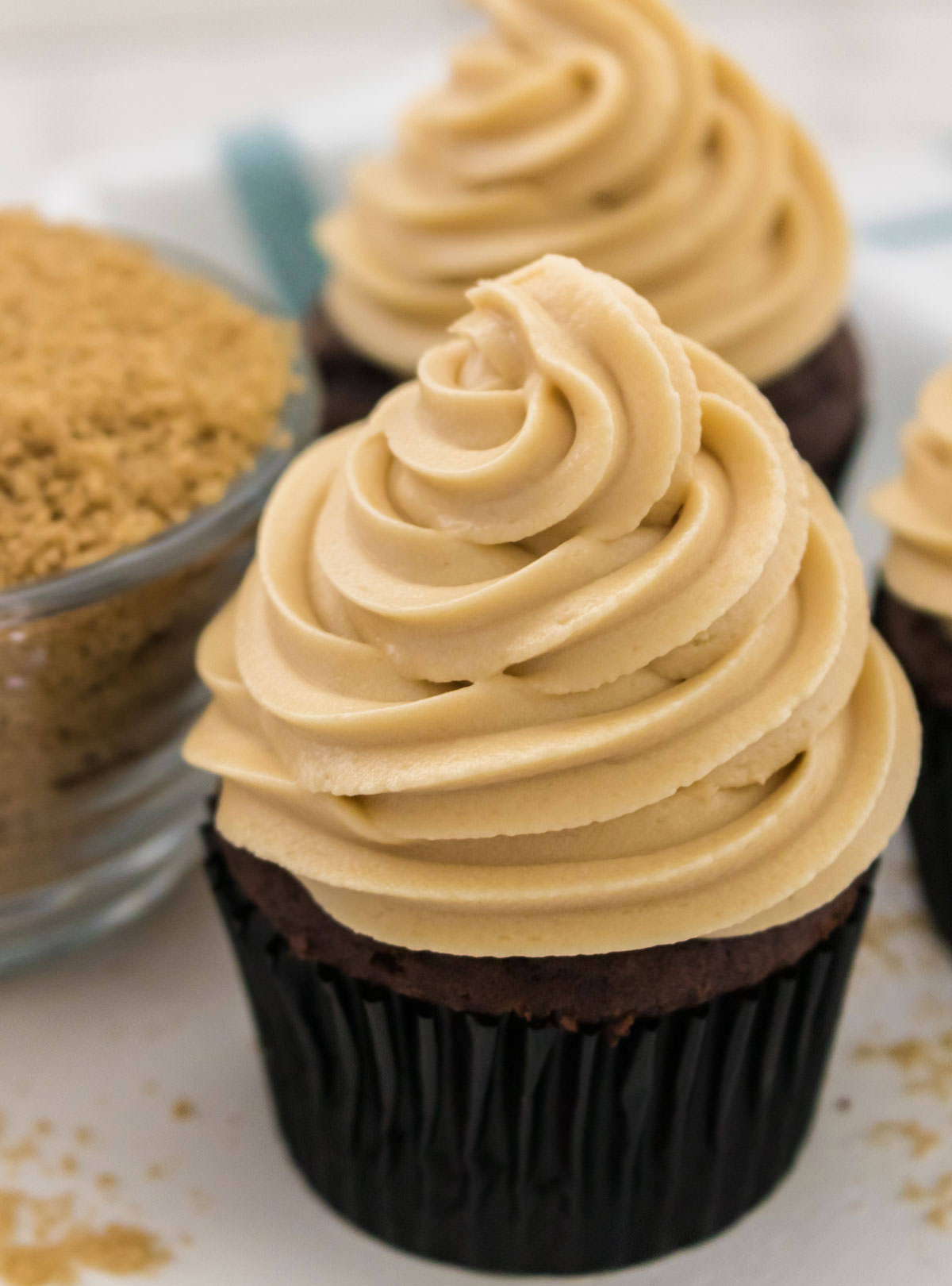Closeup of a chocolate cupcake topped with The Best Brown Sugar Cream Cheese Frosting sitting next to a bowl of brown sugar.