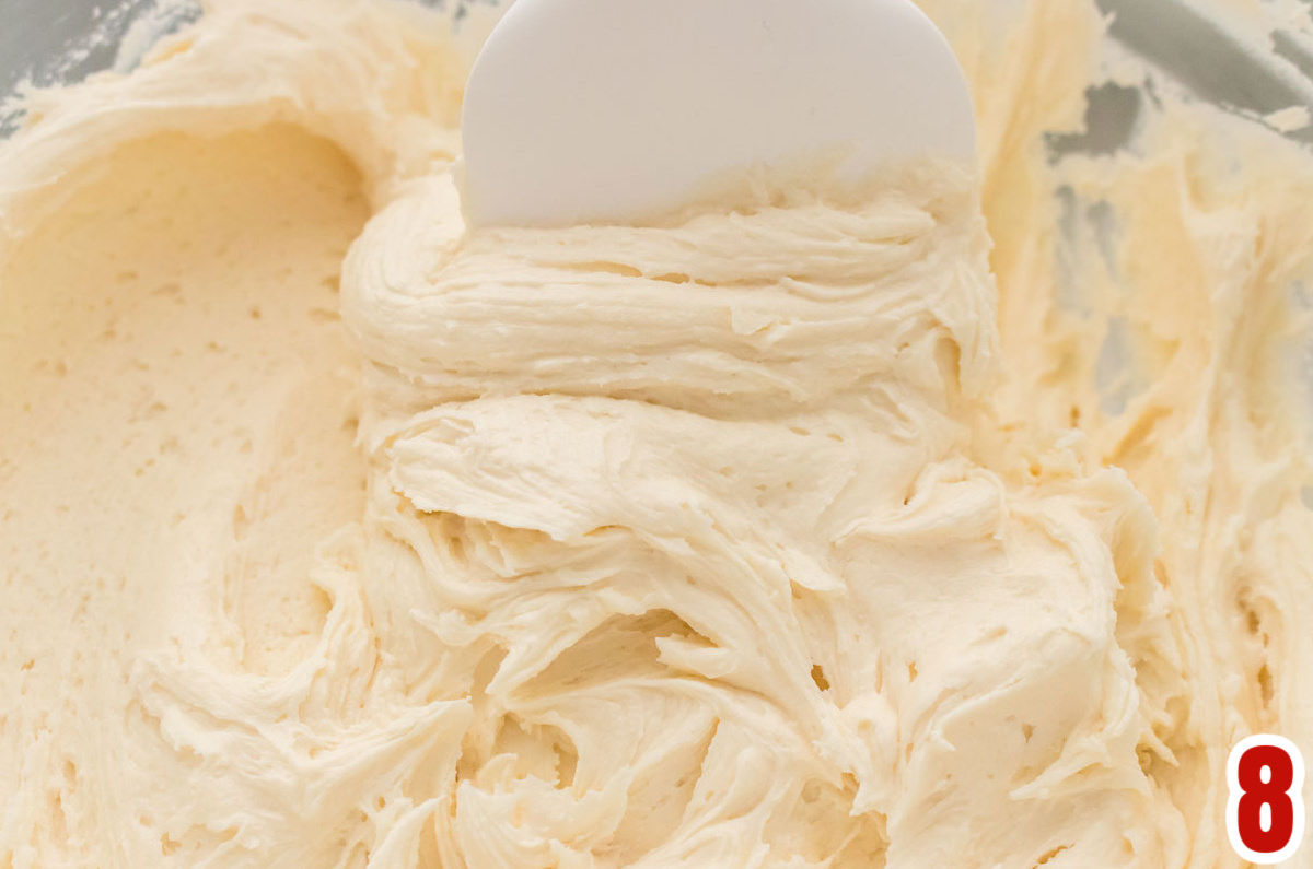 Closeup on a clear glass mixing bowl filled with Buttercream Frosting and a White spatula.