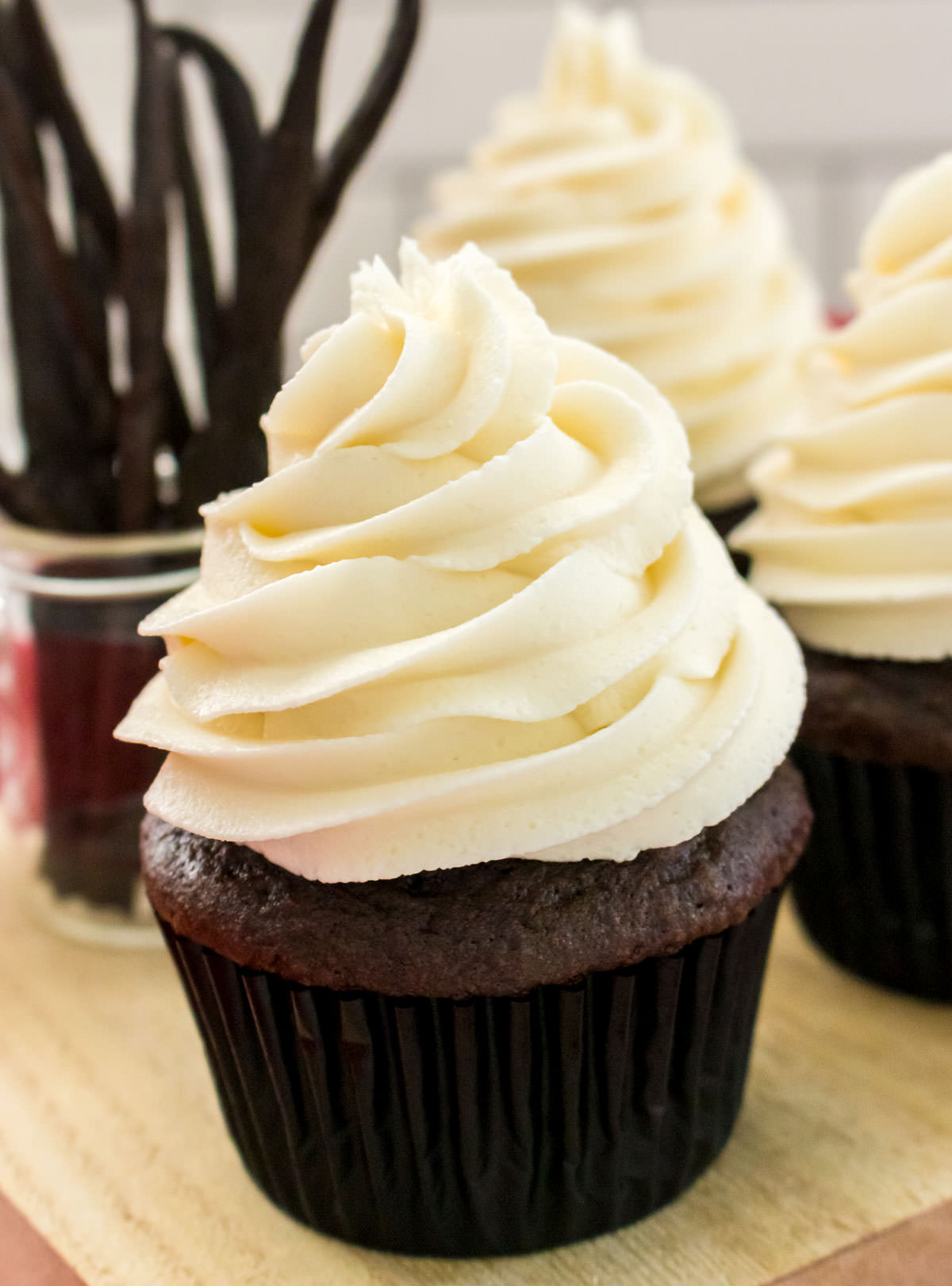 Closeup on a chocolate cupcake topped with The Best Buttercream Frosting sitting on a cutting board next to a jar filled with Vanilla Beans.