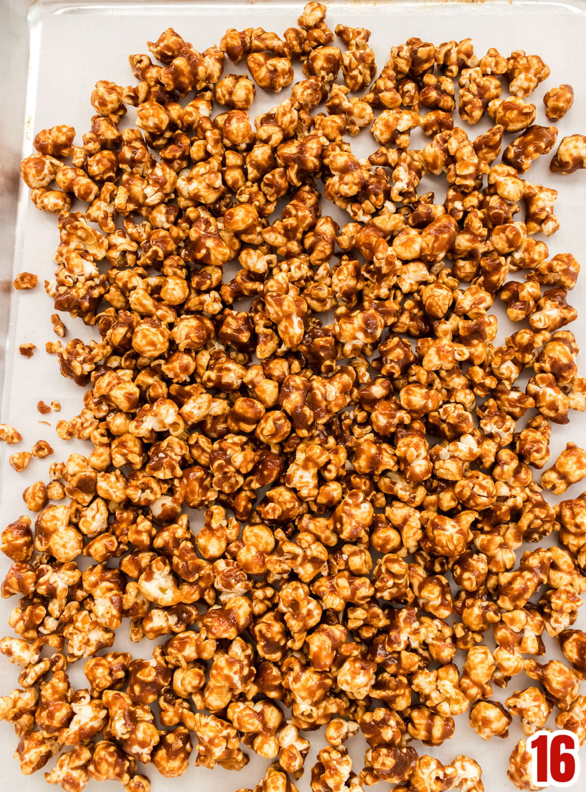 Closeup on a cookie sheet covered in parchment paper and filled with a batch of cooling Caramel Corn.