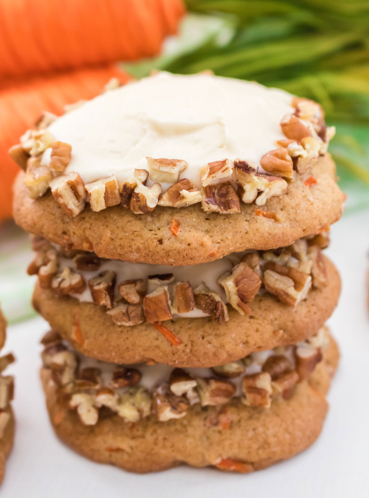 Closeup on a stack of three Carrot Cake Cookies frosted with Cream Cheese Frosting and decorated with chopped pecans.