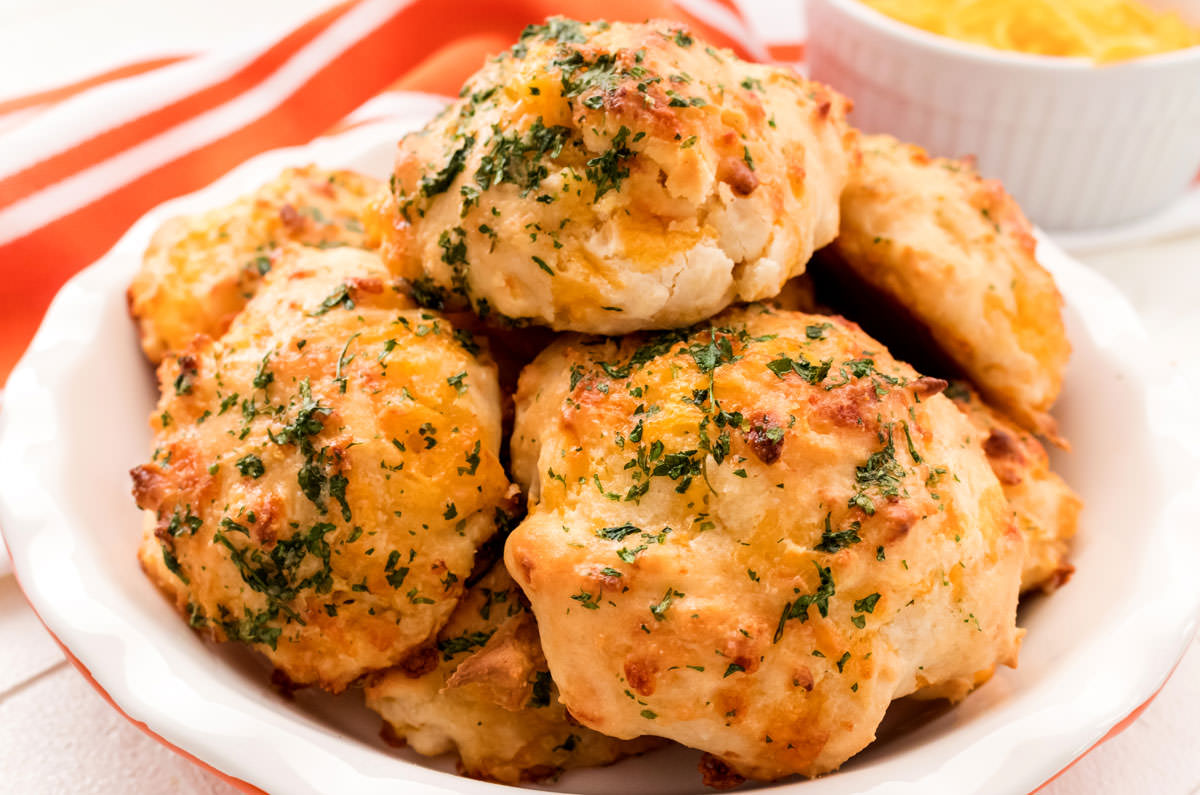 A small pie plate sitting on a white table and filled with Cheesy Garlic Biscuits hot out of the oven.