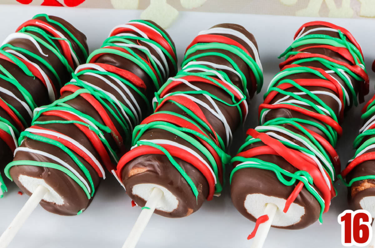 Closeup on five Christmas Marshmallow Pops laying on a white serving platter.