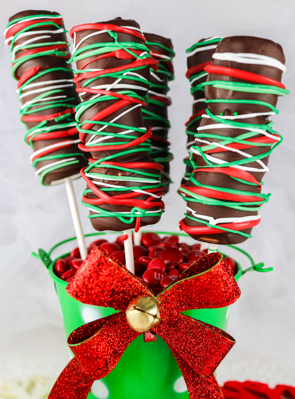 Five Christmas Marshmallow Pops sticking out of a green mini bucket with a red bow.