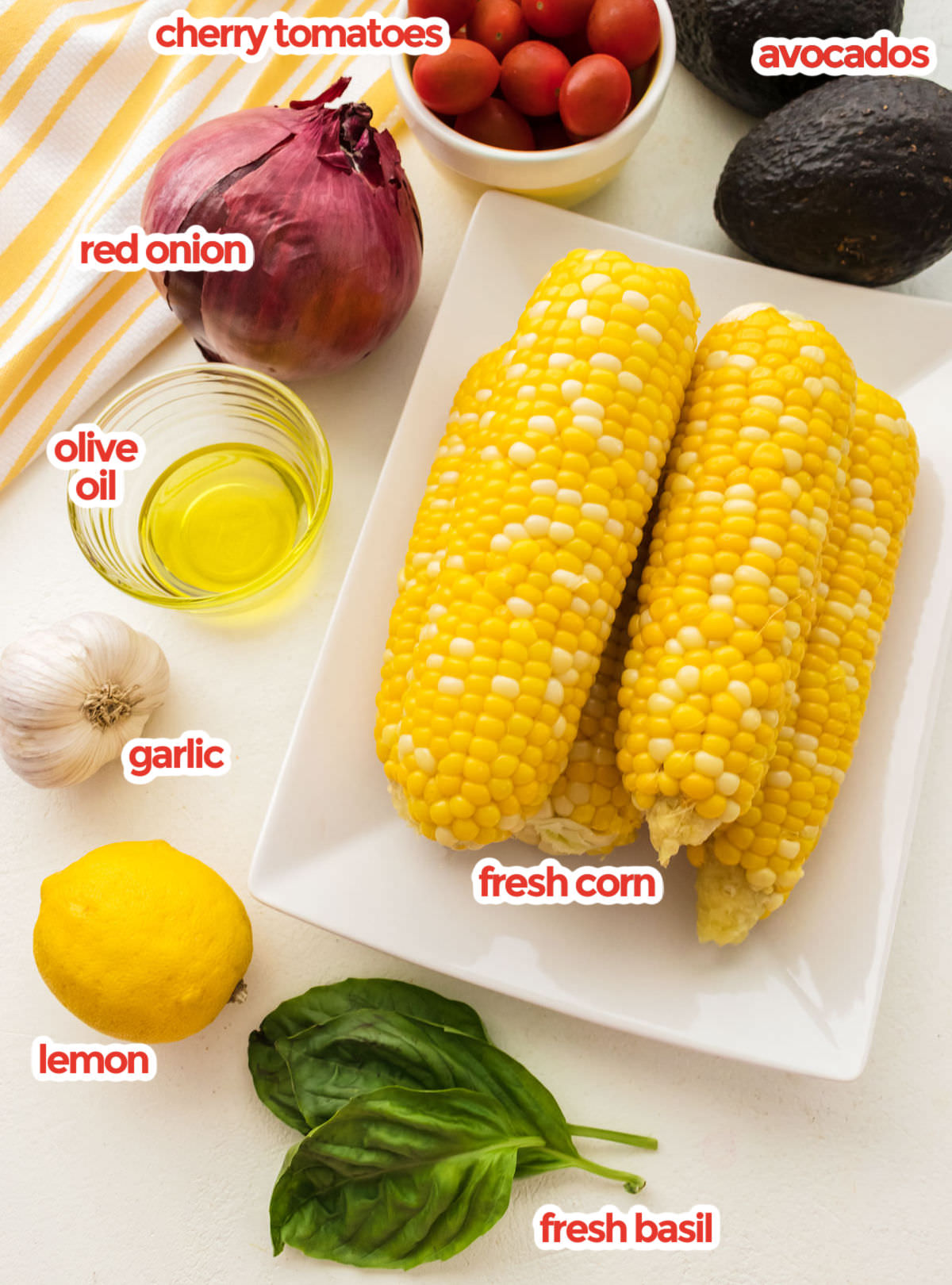 All the ingredients you will need to make Summer Corn Salad including corn, avocados, cherry tomatoes, red onion, olive oil, garlic, lemon and fresh basil.