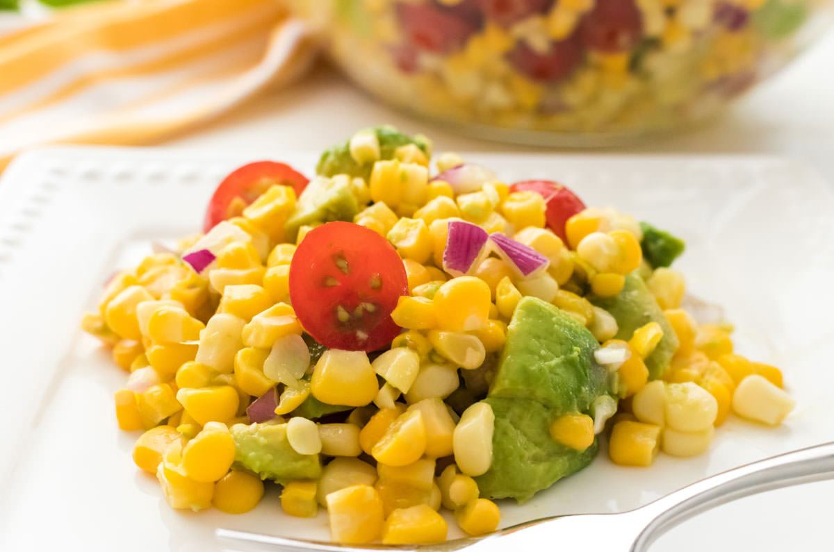 Close up on a white salad plate filled with The Best Ever Summer Corn Salad sitting in front of a glass bowl filled with Corn Salad.