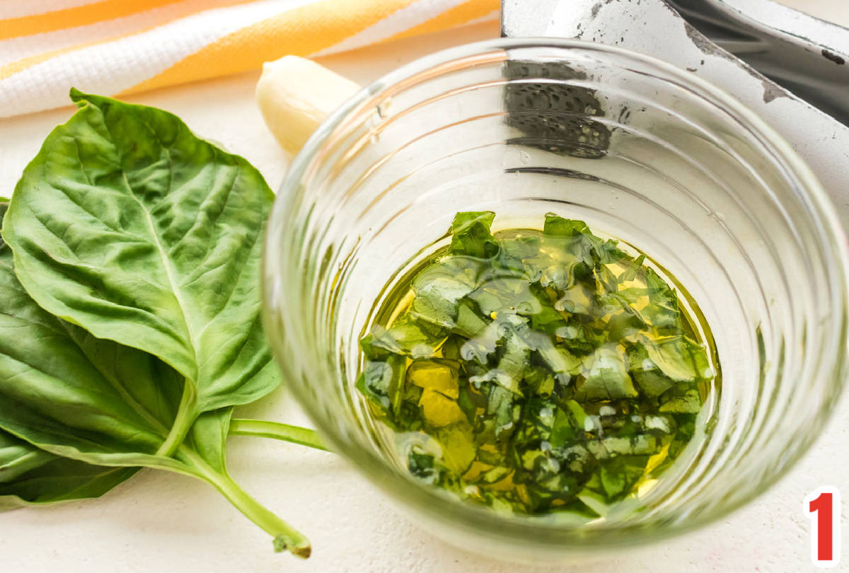 Closeup on a bowl of Garlic Basic Salad Dressing next to fresh basil leaves and a garlic press.