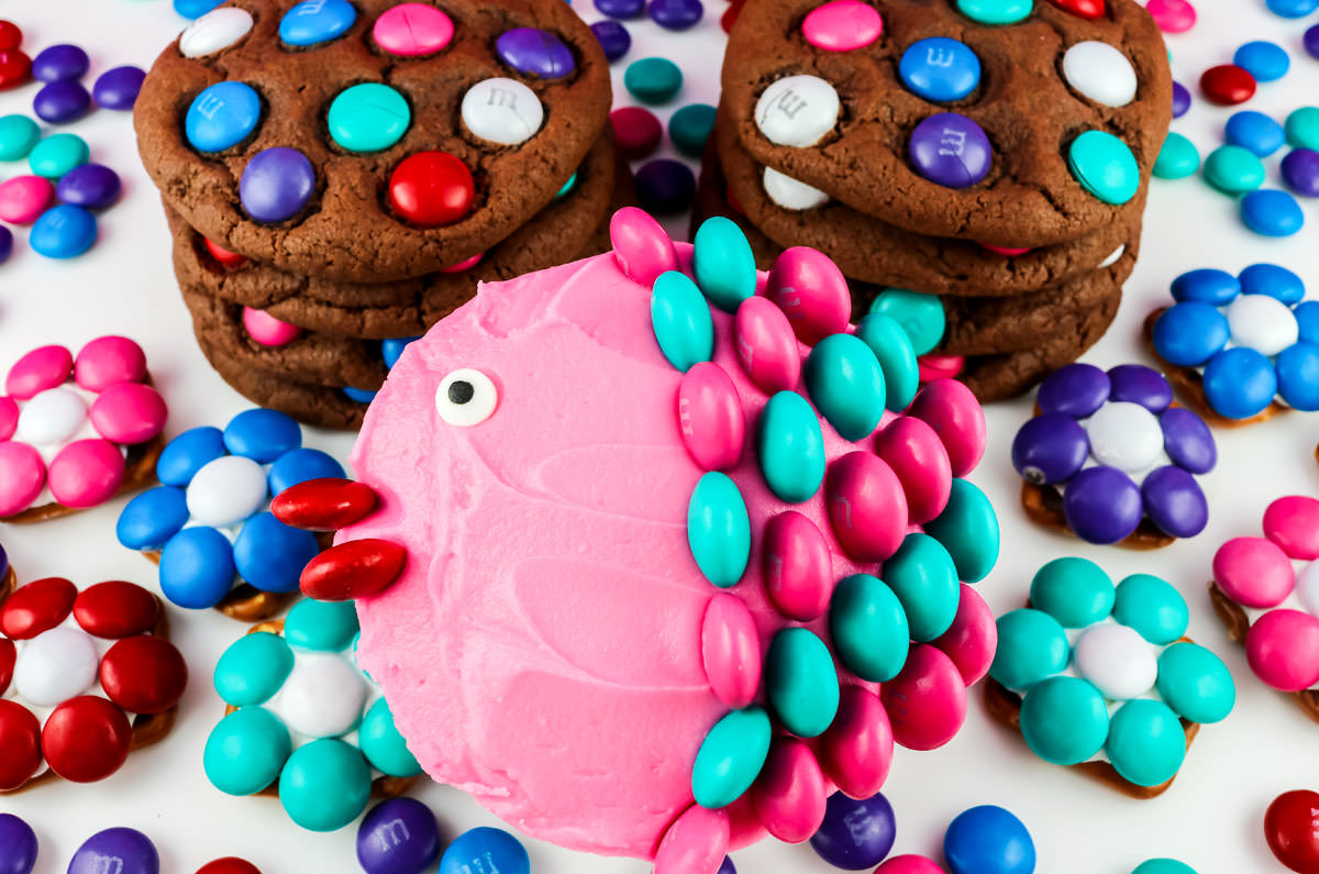 Overhead shot of cupcakes, cookies and pretzel bites decorated with colored M&M's.