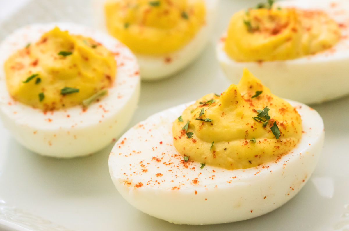 Closeup on four Homemade Deviled Eggs garnished with paprika and parsley flakes sitting on a white plate.