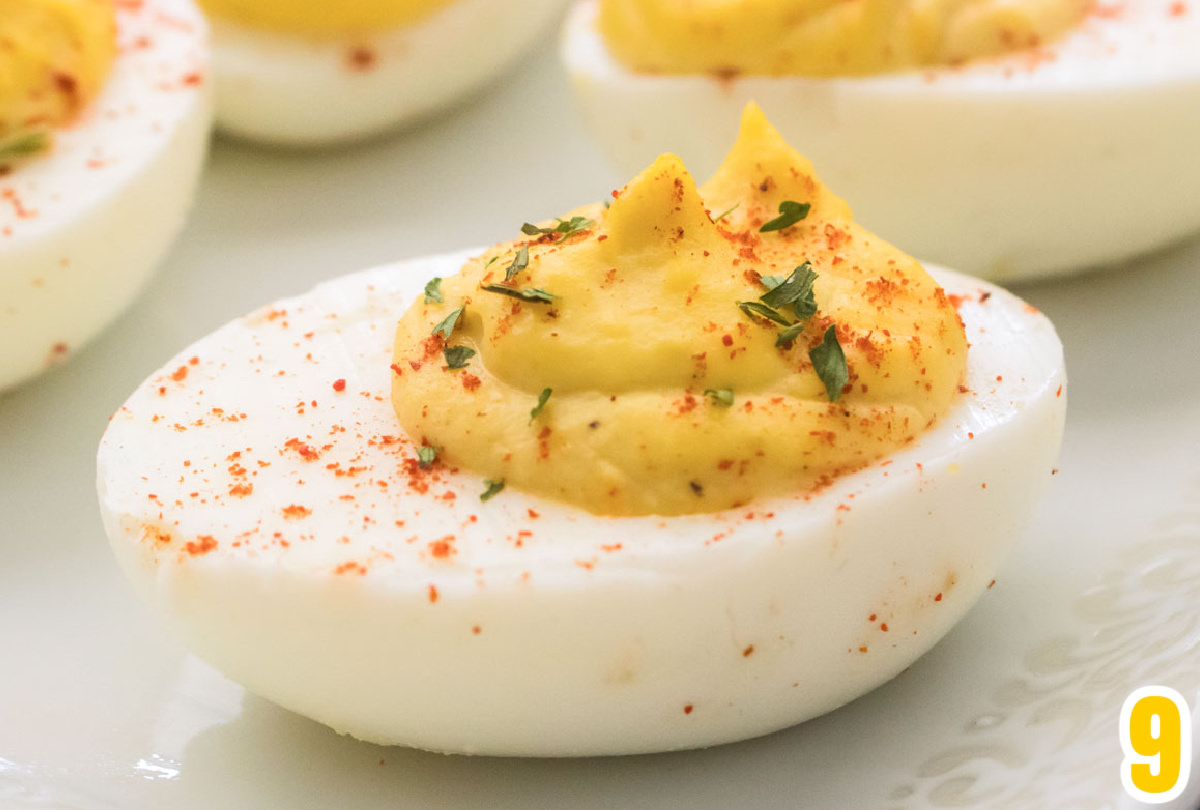 Closeup on a single Deviled Egg garnished with paprika and parsley on a white plate.