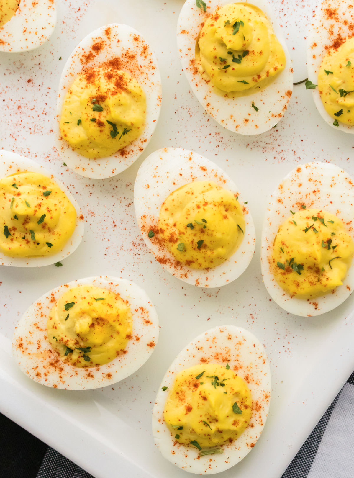 Closeup on a white serving platter filled with Deviled Eggs garnished with paprika and parsley.