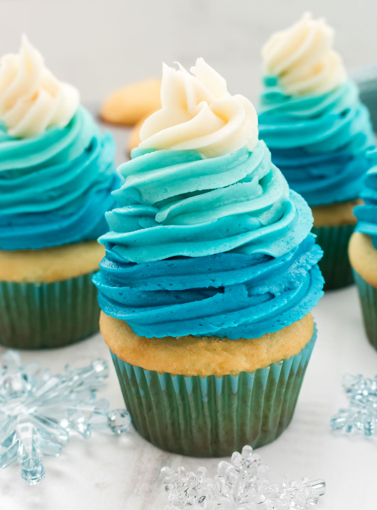 Closeup of a Frozen Ombre Swirl Cupcake sitting on a white surface surrounded by snowflake decorations.