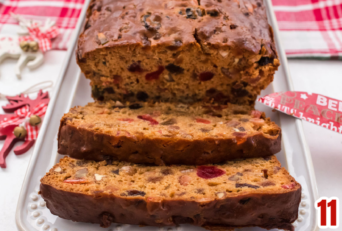 Closeup on a loaf of Fruit Cake on a white serving platter surrounded by Christmas decorations.