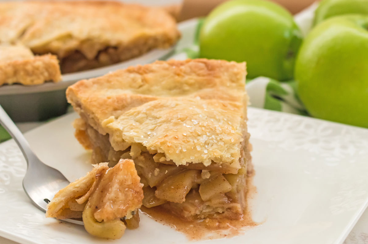 Closeup on a single piece of Homemade. Apple Pie sitting on a white dessert plate with a piece of pie on a fork next to it.