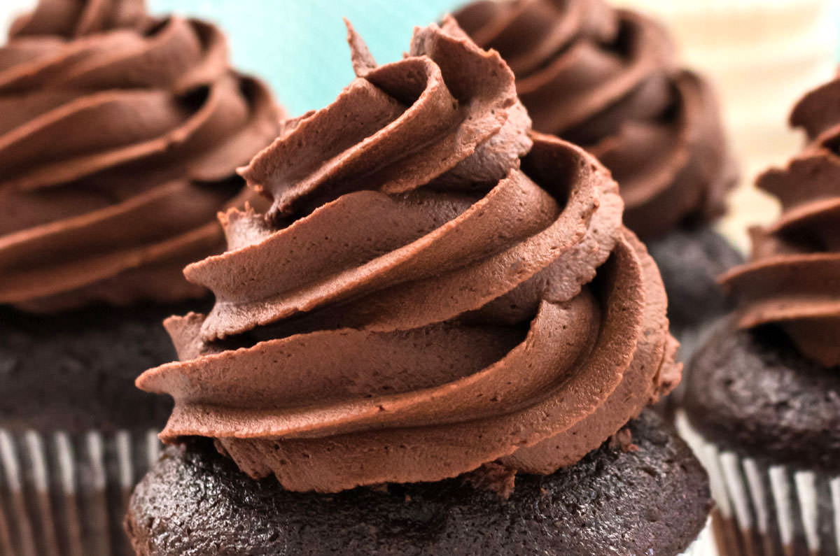 Closeup on a tall swirl of Chocolate Buttercream Frosting sitting on a chocolate cupcake.