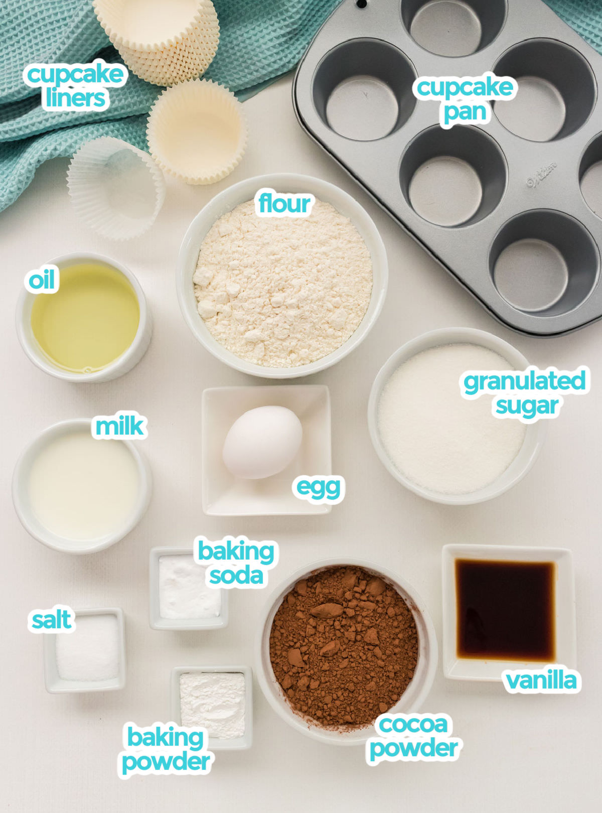 All the ingredients needed to make Homemade Chocolate Cupcakes including cupcake liners, a cupcake pan, flour, sugar, cocoa powder, oil, milk, egg, vanilla, baking soda, baking powder and salt.