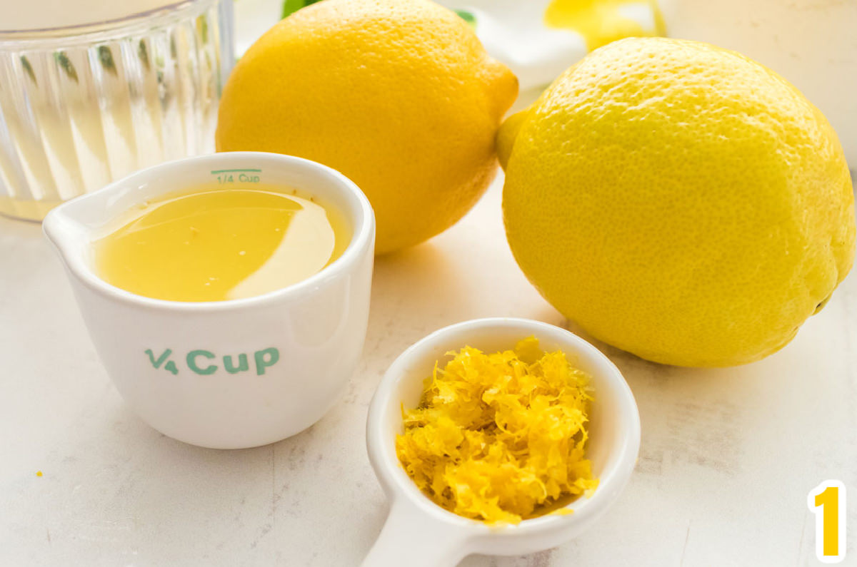 Closeup of two lemons, a measuring cup filled with lemon juice and a lemon zest.