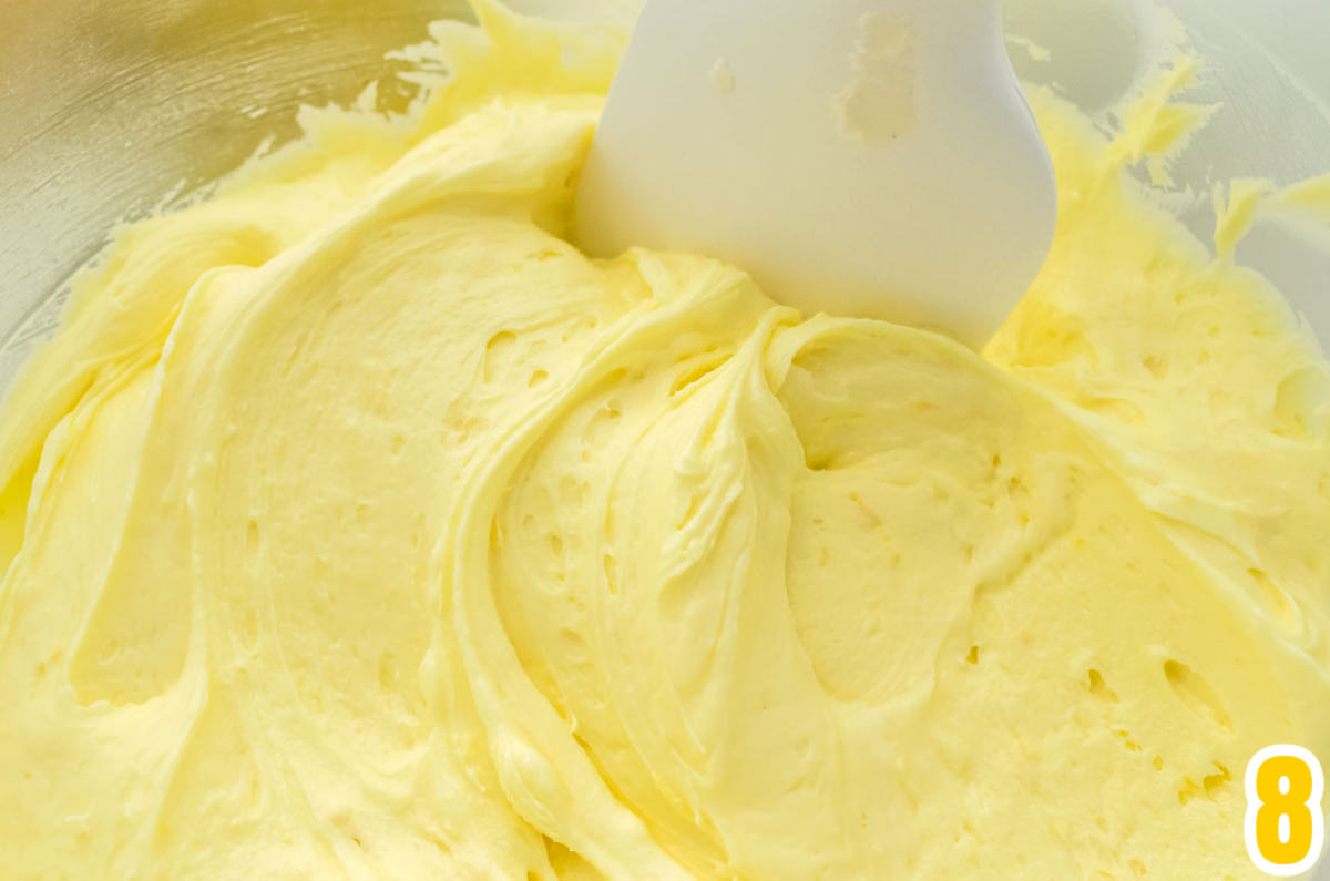 Mixing bowl filled with homemade lemon frosting with a white wooden spatula.