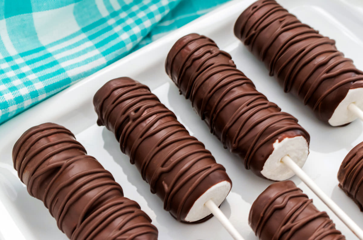 Close up on a white platter holding four marshmallow pops with an aqua kitchen linen in the background.