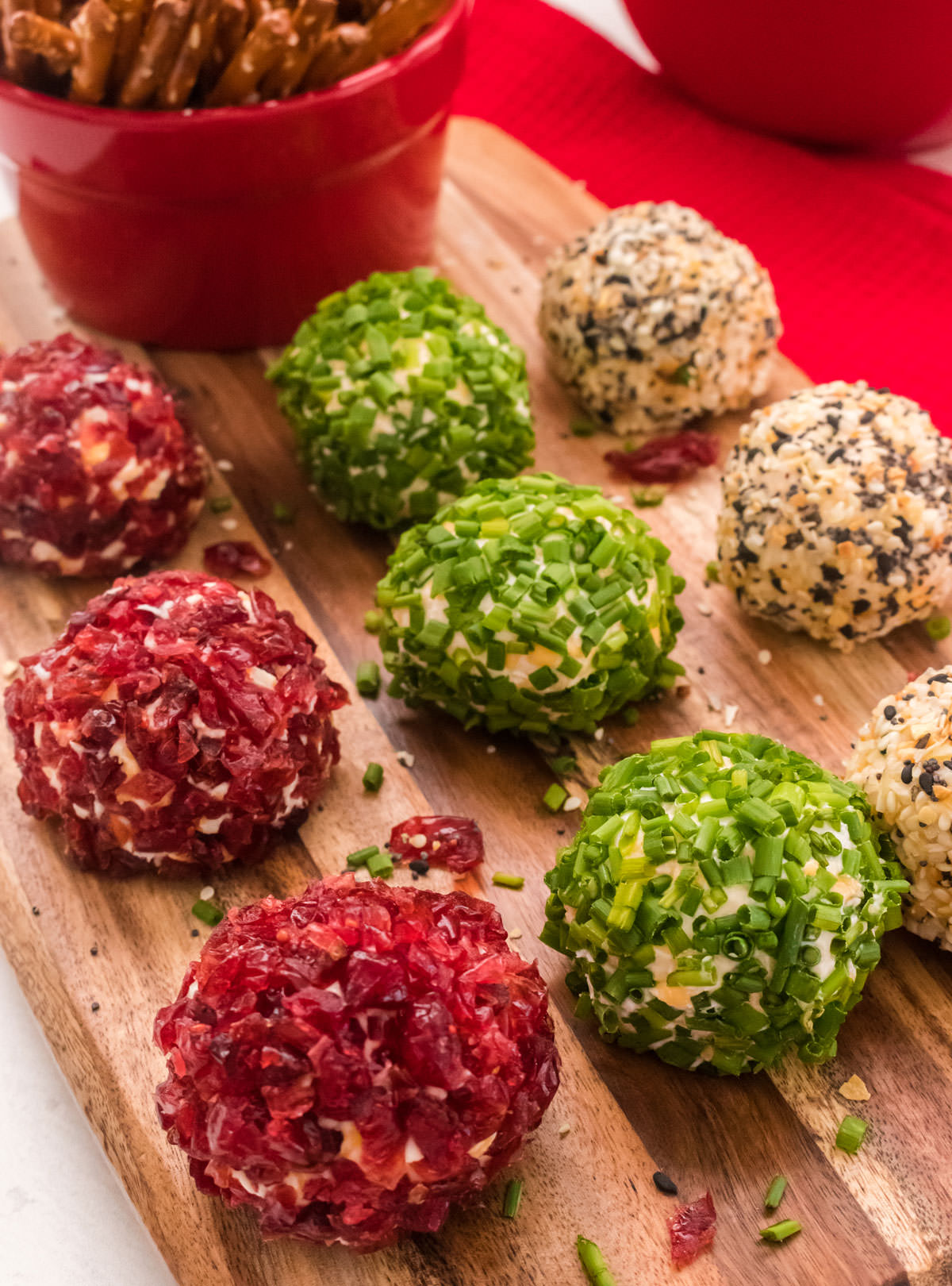 Mini Cheese Ball Bites sitting on a cutting board in front of a red ramekin filled with Pretzel Sticks. 