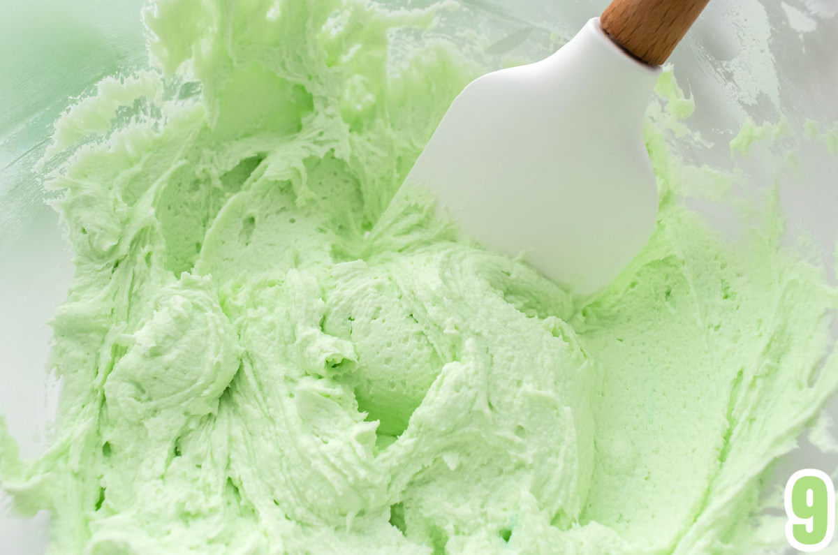 Closeup on a glass bowl filling with Homemade Mint Icing and a white wood spatula.