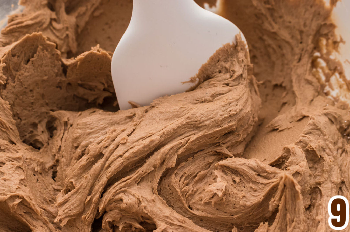 Closeup on a glass mixing bowl filled with Mocha Icing and a white spatula.