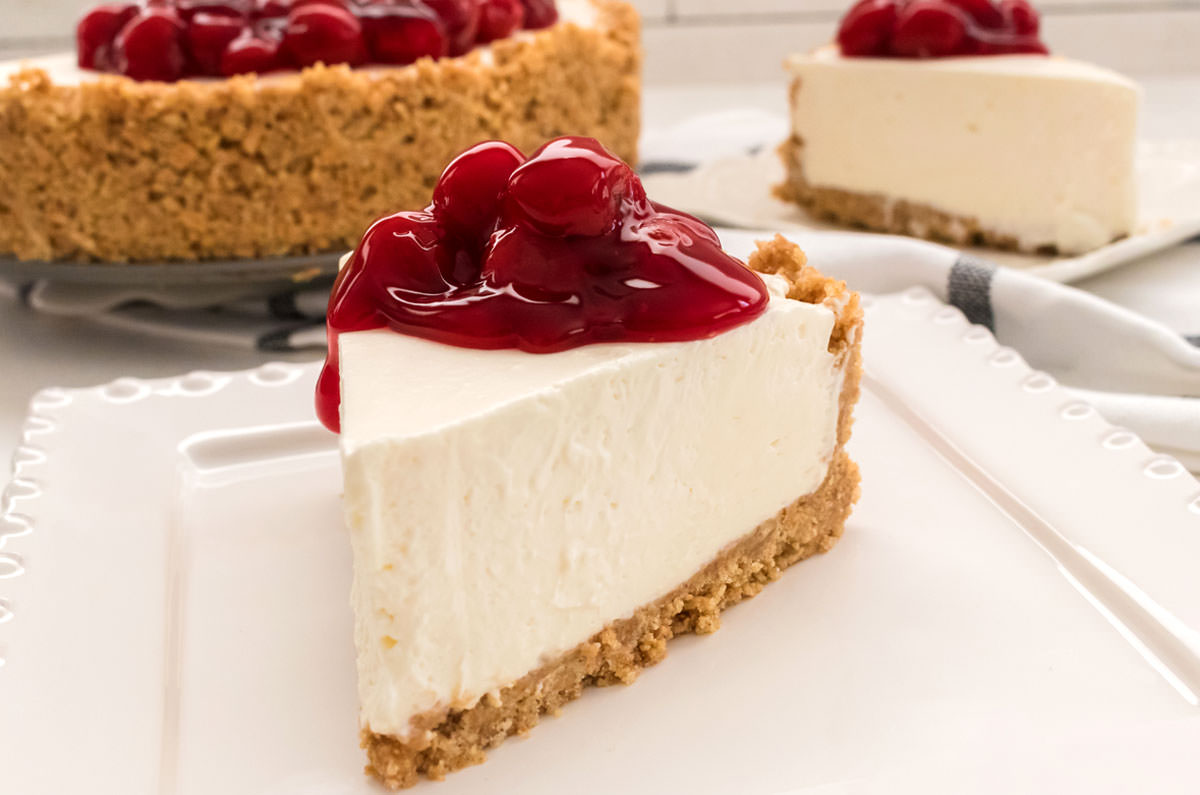 Closeup on a single piece of no bake cheese cake topped with cherry pie filling.