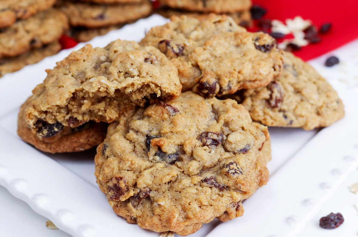 Closeup of a white plate covered with six Soft and Chewy Oatmeal Raisin Cookies in front of stacks of more Oatmeal Cookies in the background.