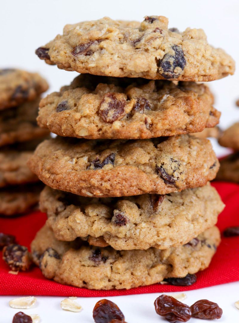 Closeup on a stack of five Soft and Chewy Oatmeal Raisin Cookies sitting on a red kitchen towel surrounded by raisins and a smattering of oatmeal.