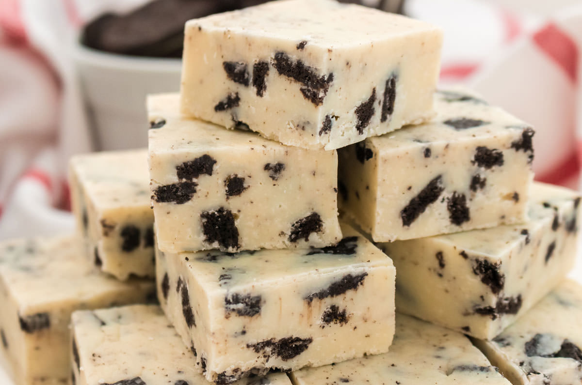 Closeup on a stack of Oreo Fudge sitting in front of a kitchen towel and a white bowl filled with Oreo Cookies.