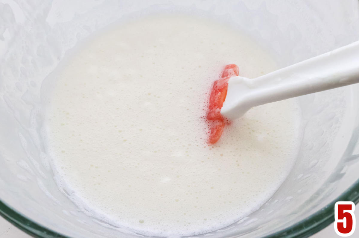 Closeup on a glass mixing bowl filling with melted marshmallows and milk.