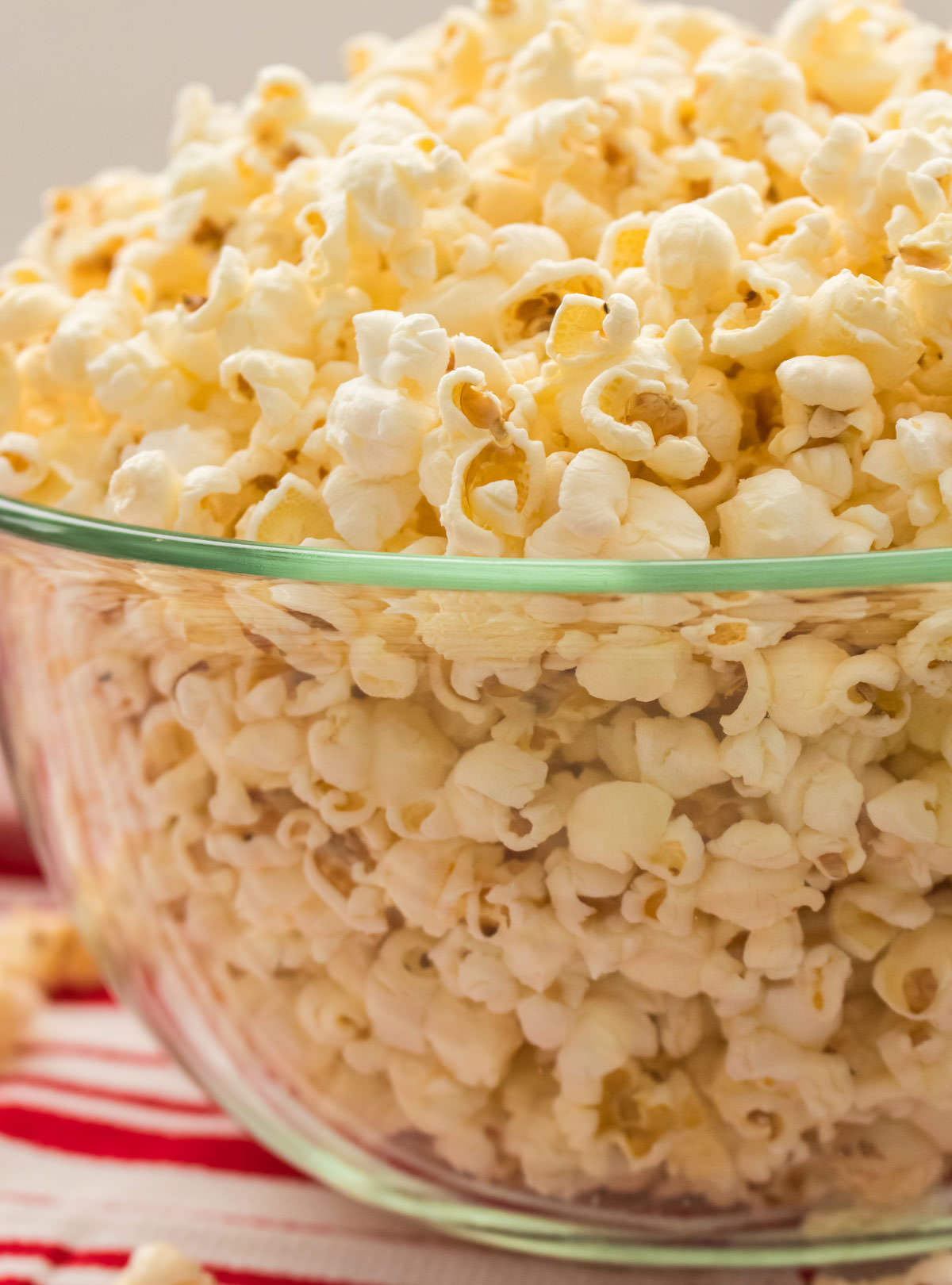 Closeup on a glass serving bowl filled with popcorn made on a stovetop sitting on a red and white table linen.