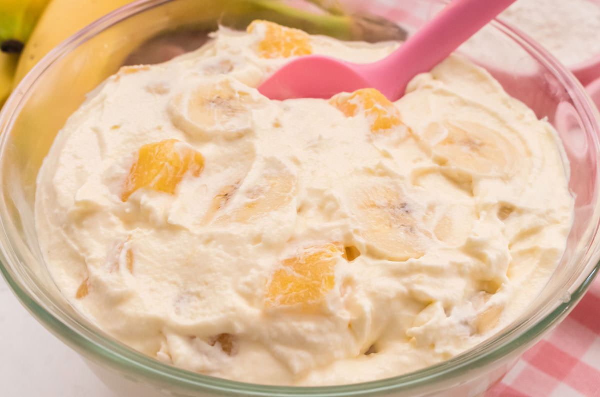 Close up on the top of a glass bowl filled with chilled Pineapple Banana Fluff sitting on a pink table linen.