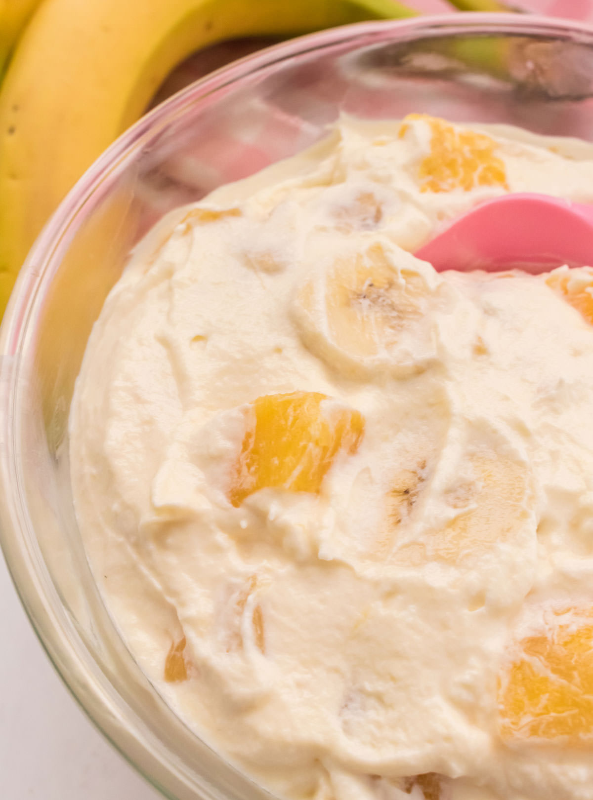 Closeup on a glass bowl filled with Pineapple Banana Fluff with a banana and a pink table linen in the background.