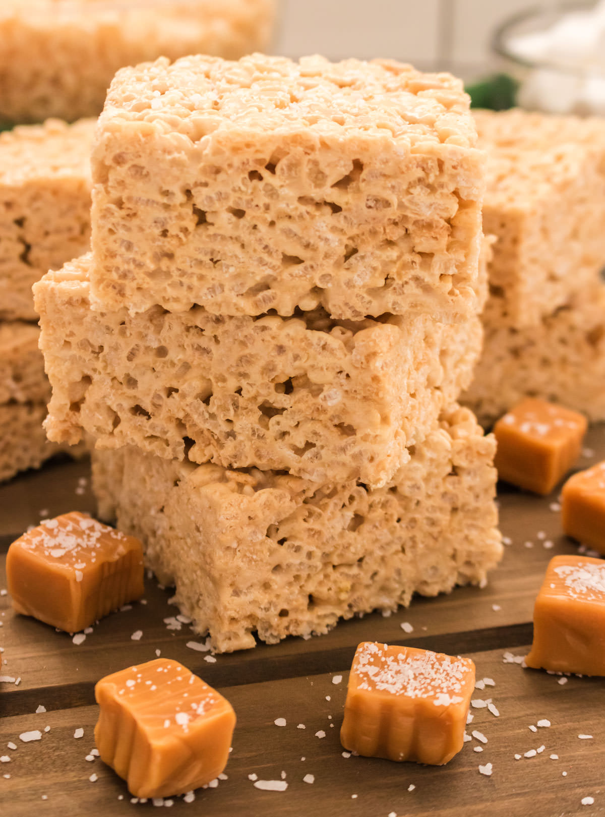Closeup on a stack of The Best Salted Caramel Rice Krispie Treats sitting on a cutting board surrounded by Caramel candies and sea salt.