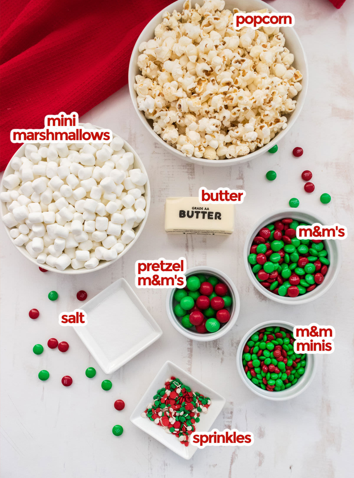 All the ingredients you will need to make Santa Crunch Popcorn including popcorn, mini marshmallows, butter, salt, sprinkles and various types of Red and Green M&M's.