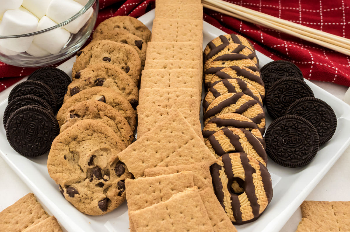 A white serving platter filled with graham crackers, chocolate chip cookies, Oreo cookies and Fudge Stripes Cookies.