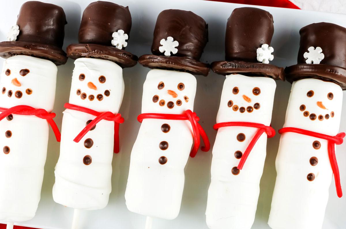 Closeup on a batch of Snowman Marshmallow Pops laying on a white serving platter.
