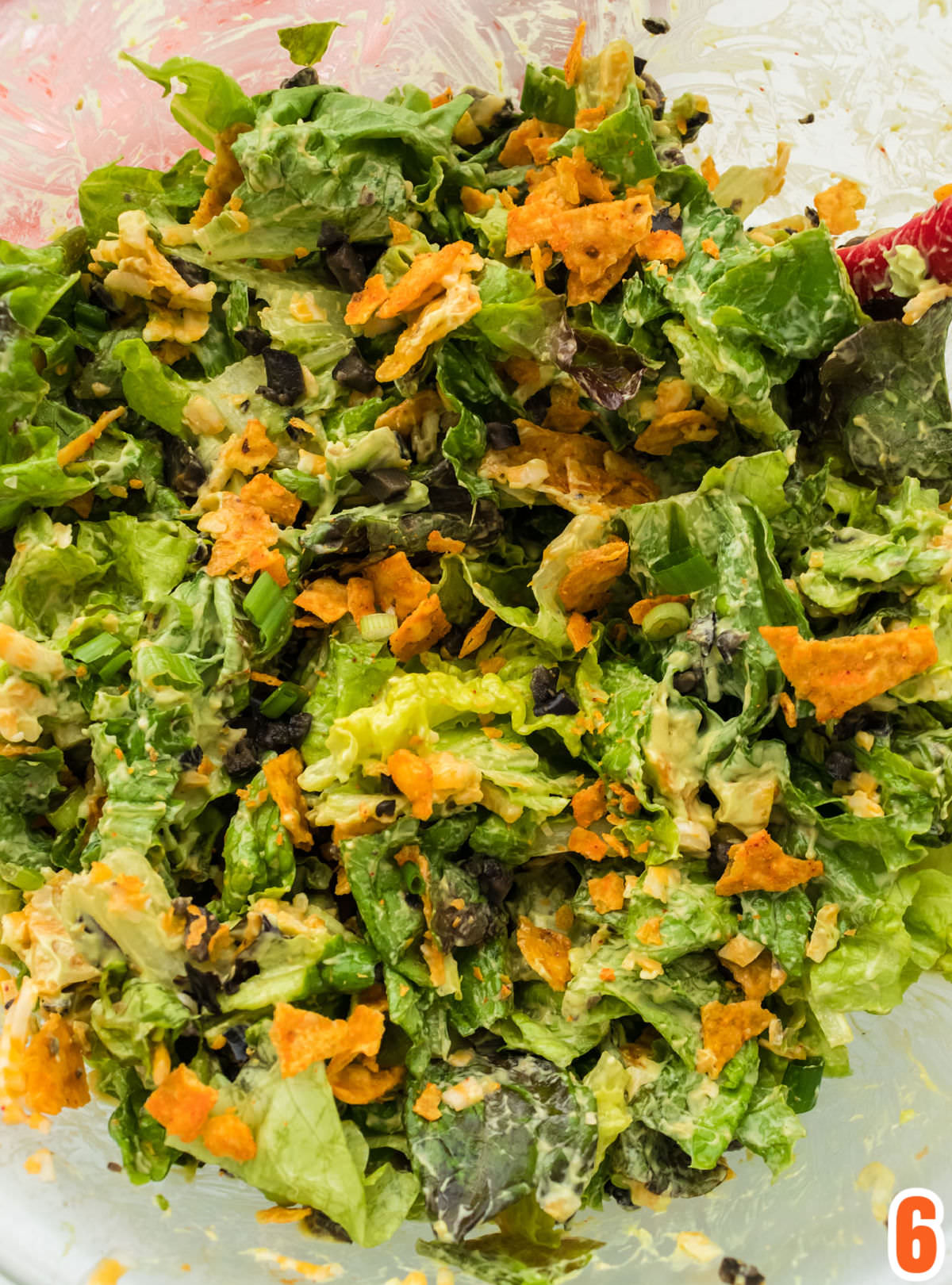 Closeup on a glass bowl filled with Dorito Taco Salad dressed with Homemade Avocado Dressing and chock full of Nacho Cheese Doritos.