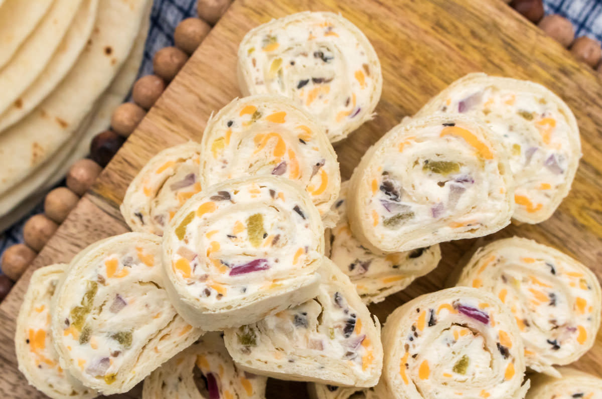 Closeup on a stack of Tortilla Pinwheels sitting on a cutting board next to a stack of flour tortillas.