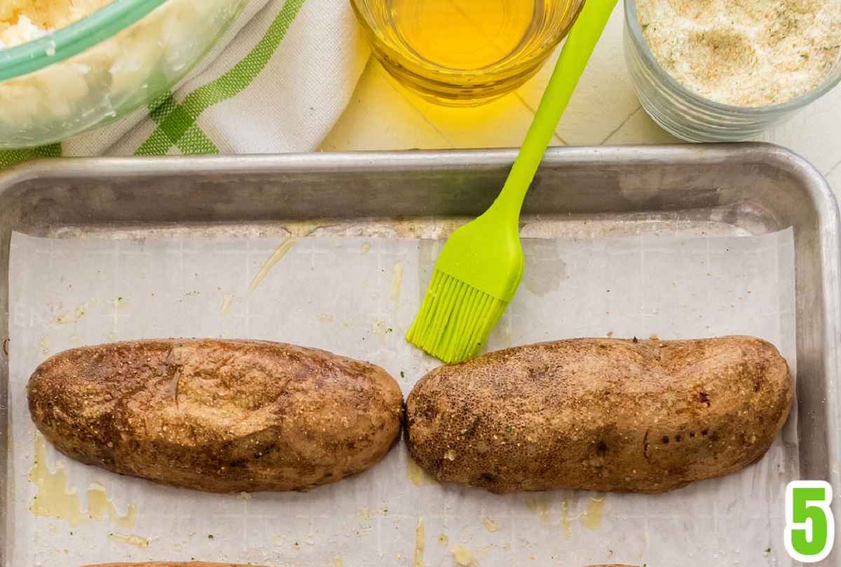 Closeup of a baked potato shell, upside down on a cookie sheet ready to go back in the oven after being lightly brushed with olive oil.