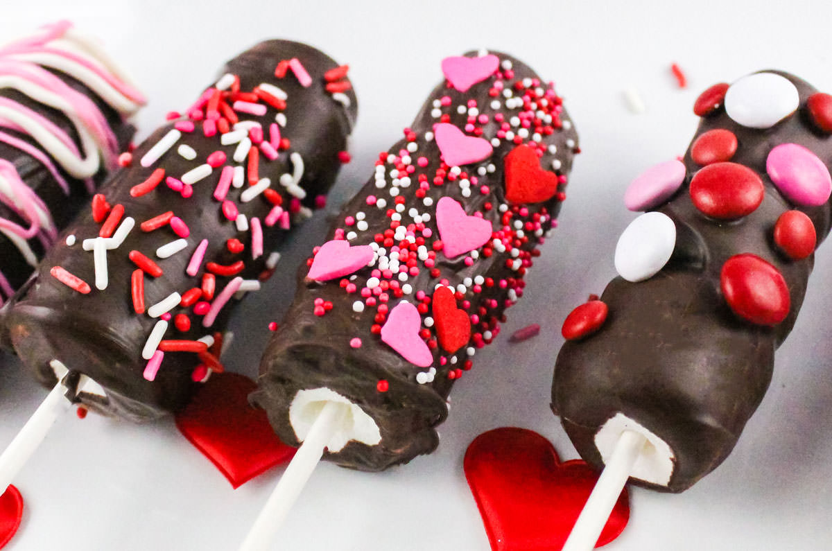 Closeup of three Valentine's Day Marshmallow Pops decorated with red, white and pink sprinkles, hearts and M&M's.