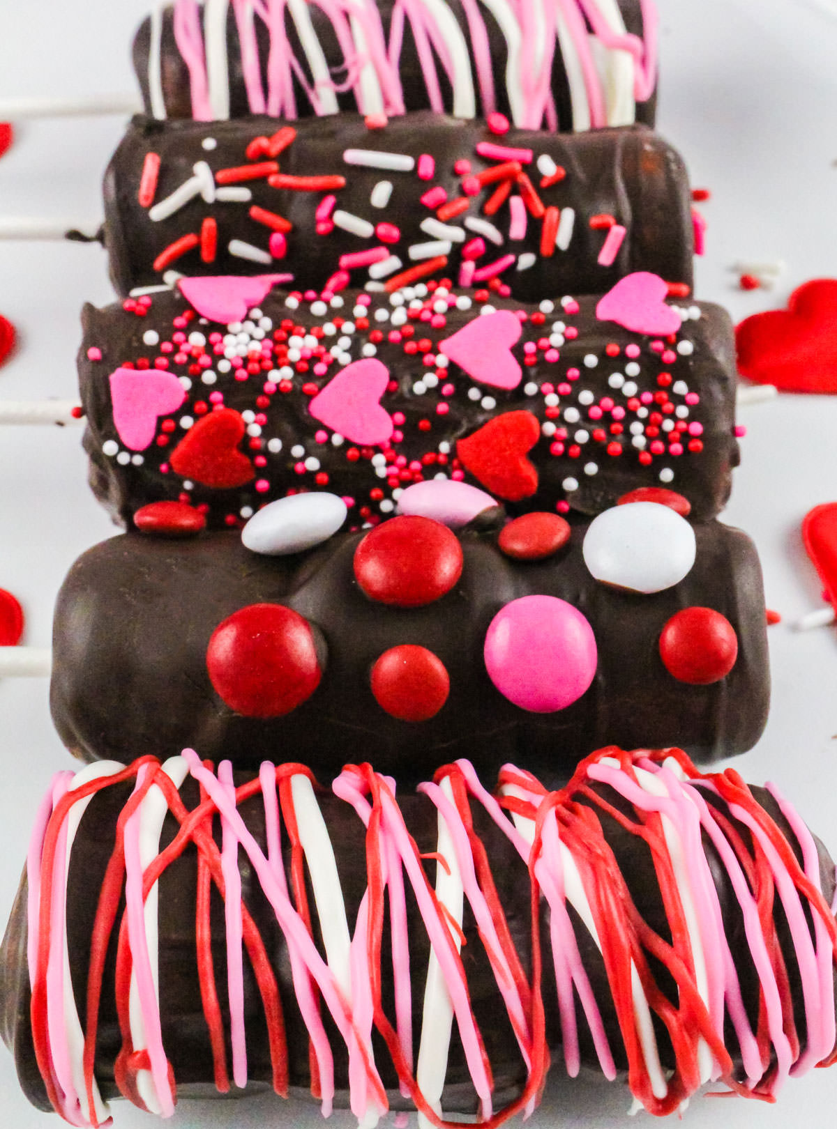 Five Valentine's Day Marshmallow Wands on a white serving platter, decorated in Valentine's M&M's, sprinkles and candy.