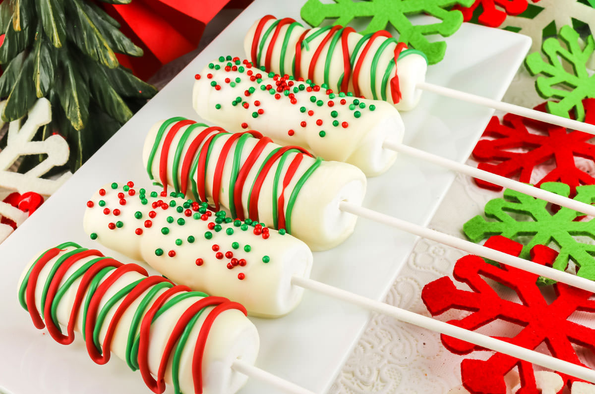 Closeup on a white serving platter covered with five White Chocolate Marshmallow Pops surrounded by Christmas decor.