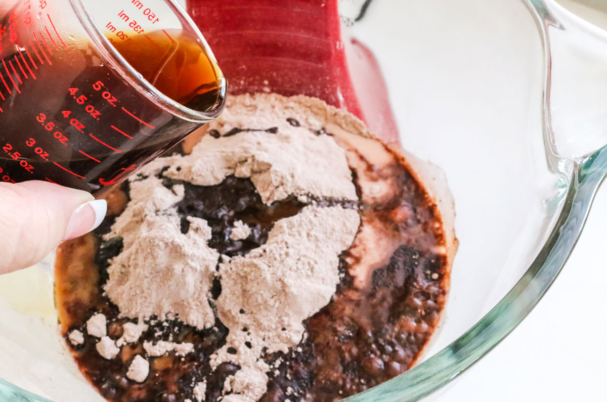 Pouring coffee into a mixing bowl filled with chocolate cake batter.